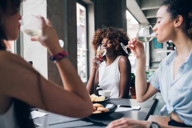 Mujeres multirraciales jóvenes sentadas en un restaurante moderno bebiendo vino juntos