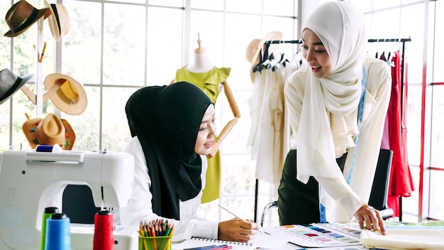 Mujeres musulmanas hermosas que bosquejan la silueta de la ropa juntos en la oficina.