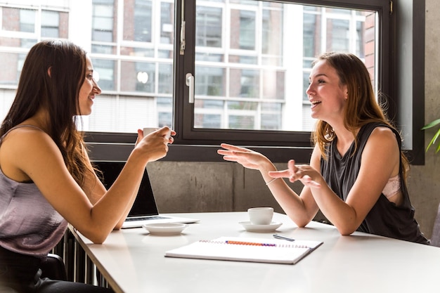 Mujeres de negocios alegres discutiendo mientras están sentadas en el escritorio en la oficina