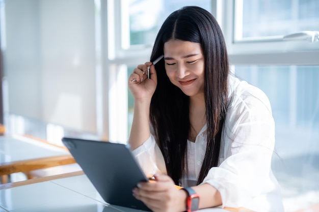 Mujeres de negocios asiáticas independientes que usan un reloj inteligente hablando haciendo un trabajo informal con una tableta para navegar por Internet, chatear y bloguear y un teléfono inteligente en una cafetería