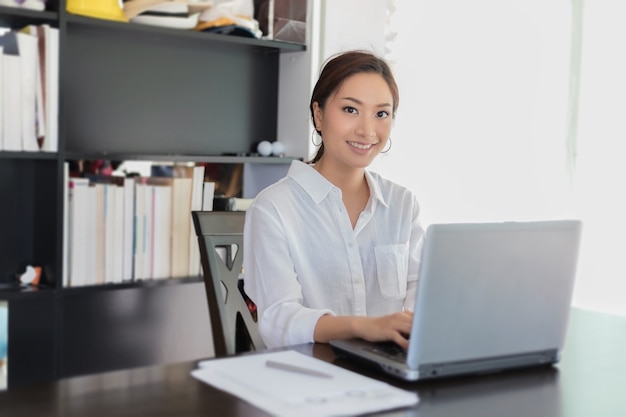 Mujeres de negocios asiáticos usando el cuaderno y sonriendo felices para trabajar en la oficina en casa