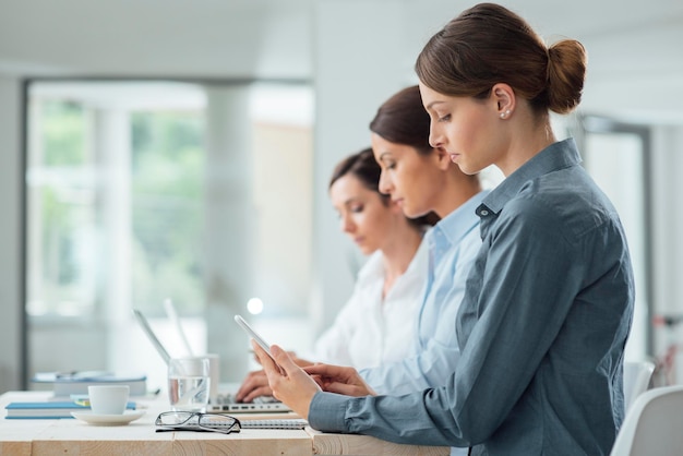 Mujeres de negocios eficientes trabajando juntas en el escritorio de la oficina usando computadoras portátiles y dispositivos móviles concepto de mujeres empresarias