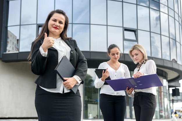 Mujeres de negocios hermosas y jóvenes con documentos y carpetas posando fuera del edificio de oficinas