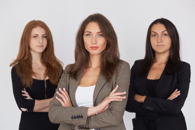 Las mujeres de negocios modernas en traje con sus brazos cruzaron la situación en fondo gris.