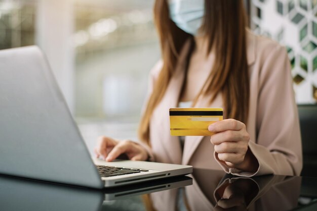 Las mujeres de negocios usan una tarjeta de crédito con una computadora portátil para pagar por Internet en la oficina por la mañana