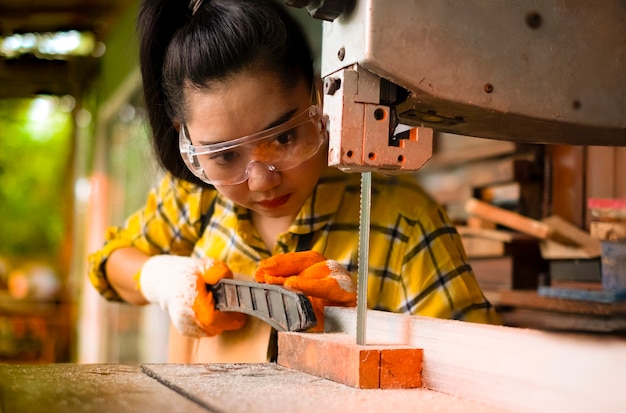 Las mujeres de pie es madera cortada de trabajo artesanal en un banco de trabajo con sierras de cinta herramientas eléctricas