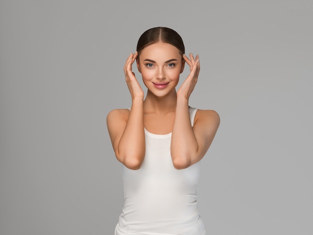 Mujeres de la piel sana de la belleza que tocan el retrato cosmético del estudio de la cara. Ropa deportiva color fondo gris