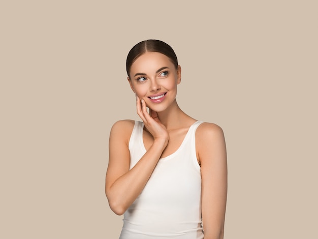 Mujeres de la piel sana de la belleza que tocan el retrato cosmético del estudio de la cara. Ropa deportiva color fondo marrón