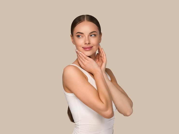 Foto mujeres de la piel sana de la belleza que tocan el retrato cosmético del estudio de la cara. ropa deportiva color fondo marrón