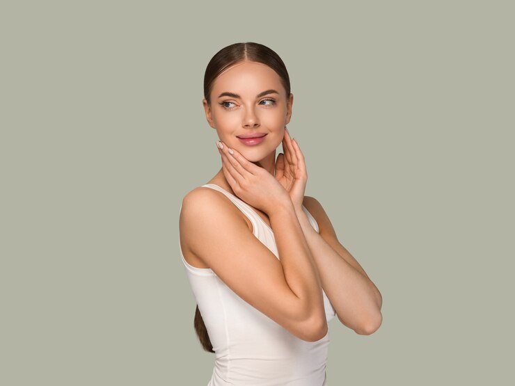 Foto mujeres de la piel sana de la belleza que tocan el retrato cosmético del estudio de la cara. ropa deportiva color fondo verde