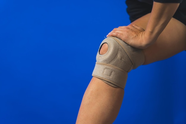 Mujeres con una pierna con un soporte protector de rodilla con fondo azul conceptos de lesión y dolor