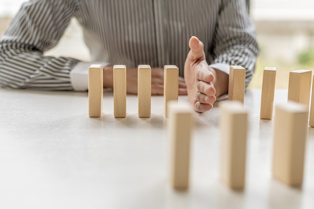 Las mujeres ponen sus manos entre bloques de madera, bloques de madera dispuestos en dominó, comparados con el buen funcionamiento de un negocio y la resolución de problemas. El concepto de gestión empresarial en riesgo.