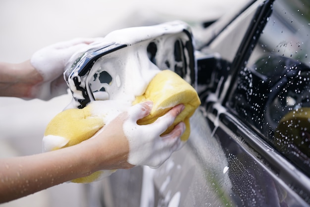 mujeres que lavan un coche gris jabonoso con una esponja amarilla.