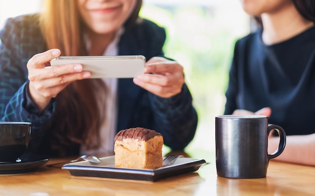 Las mujeres que utilizan el teléfono móvil para tomar una foto de la torta y el café antes de comer en la cafetería