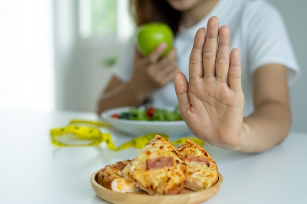 Las mujeres rechazan y empujan pizza y comen manzanas, ensaladas de verduras colocadas frente a ellas. Las mujeres eligen alimentos saludables para el cuerpo.