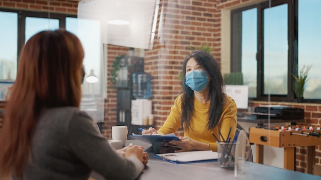 Mujeres reunidas en una entrevista de trabajo durante la pandemia de covid 19. Empleado de negocios hablando con el candidato sobre información laboral y reclutamiento, usando mascarilla en la oficina de la empresa.