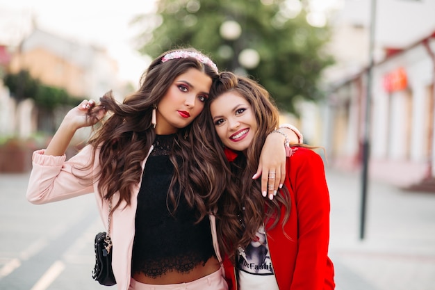 Mujeres riendo en trajes deportivos elegantes y bolsos en la calle.