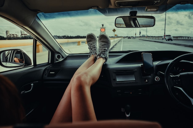 Mujeres sentadas en el asiento del pasajero en el coche con los pies en el salpicadero. Mujer joven relajante en coche. en vacaciones de viaje de verano. concepto de viaje.