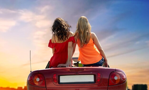 mujeres sentadas en un coche descapotable sobre la ciudad al atardecer