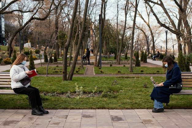 Foto mujeres sentadas a distancia y con máscara