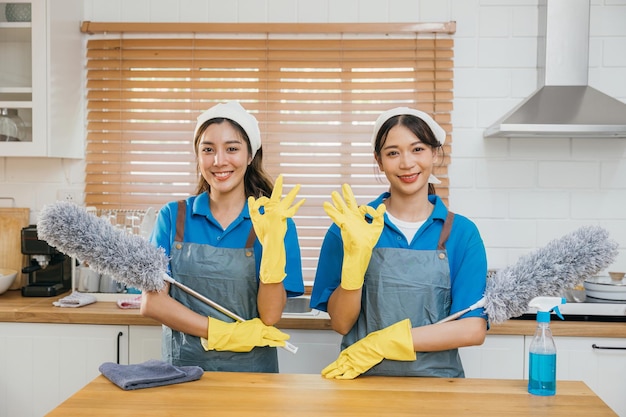 Mujeres de servicio de limpieza en uniforme de pie en el mostrador de la cocina sosteniendo el polvo spray y trapo con niebla enfatizando el trabajo en equipo en el trabajo doméstico eficiente retrato limpio dos criadas de uniforme trabajando empleado sonriente