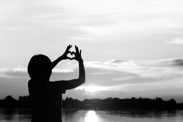 las mujeres de la silueta usan su mano hacen la forma del corazón con puesta de sol.