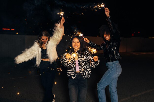 Mujeres sonrientes con chispas bailando al aire libre