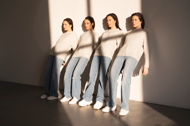 Foto mujeres en suéteres y jeans apoyados contra la pared a la sombra de la ventana