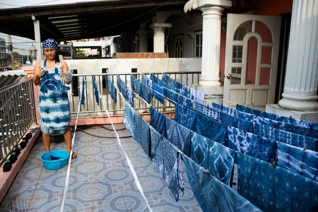Mujeres tailandesas que trabajan en el conocimiento indígena de Tailandia atan batik teñido de color índigo o color mauhom y proceso de colgar tela seca al sol al aire libre en la parte superior de la casa en Nonthaburi Tailandia