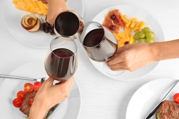 Mujeres tintineando copas con vino y deliciosos platos en la mesa en el restaurante