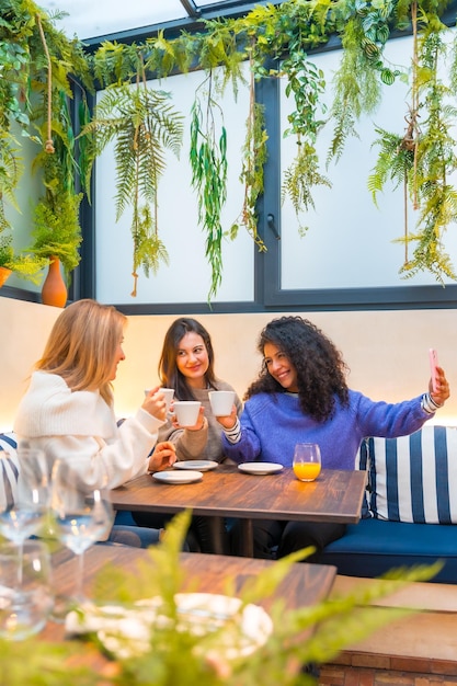 Mujeres tomando selfie sentadas juntas en una cafetería