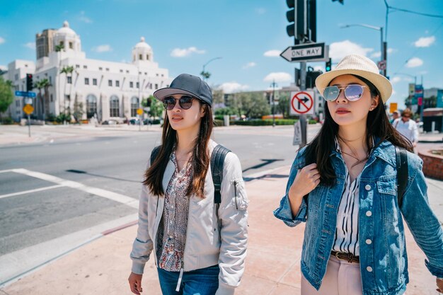 mujeres turistas caminando por la calle con sombreros y gafas de sol en un día soleado. chicas jóvenes caminando hacia el siguiente lugar turístico en Los Ángeles. Feliz viaje juntos de hermanas en el centro de la ciudad.