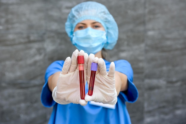 Mujeres en uniforme médico posando con tubos de ensayo con sustancia roja sobre fondo gris