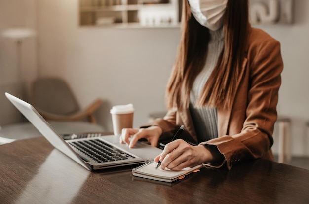 Las mujeres usan una computadora portátil y toman notas en el cuaderno en el escritorio de la oficina por la mañana