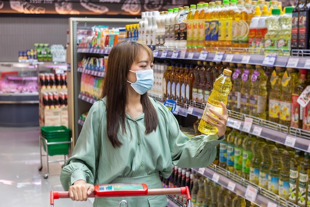 Las mujeres usan máscaras para comprar aceite de cocina en los supermercados, nuevos estilos de vida normales en la era del virus Corona o la epidemia de Covid-19