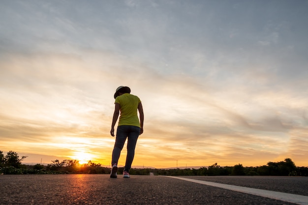 Mujeres vestidas con jeans, zapatillas y sombreros al atardecer, de pie a lo largo de la carretera para viajar