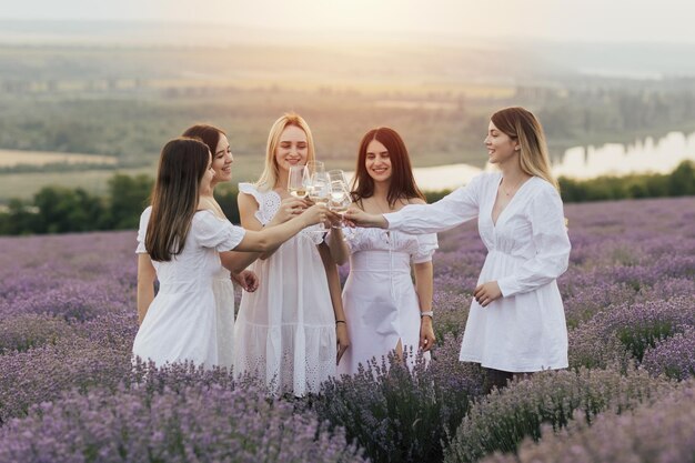 Mujeres con vestidos blancos brindando con copas de vino en un campo de lavanda