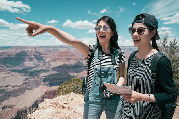 mujeres viajeras felices señalando el destino de pie en el horizonte en el parque nacional del gran cañón. las hermanas jóvenes viajan con un mapa de papel en las vacaciones de verano. gira en el concepto de estilo de vida americano.