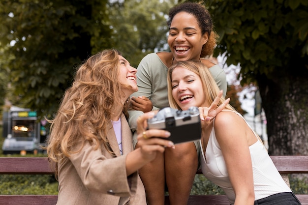 Foto mujeres de vista frontal tomando una foto del uno mismo con una cámara retro