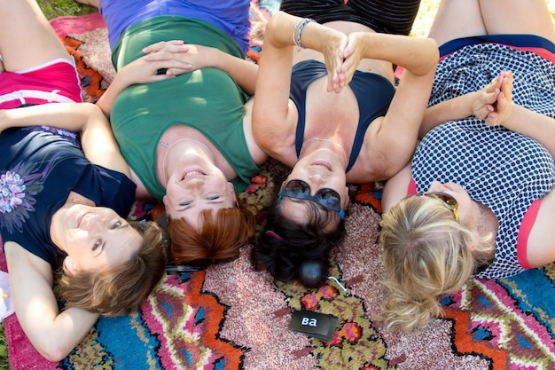 Las mujeres yacen en una manta en el parque riendo y divirtiéndose vista desde arriba