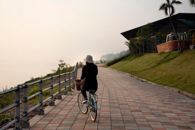 MUKDAHAN TAILÂNDIA 2 DE OUTUBRO Mulheres tailandesas andando de bicicleta na rua à beira do rio Mekhong à noite na cidade de Mukdahan em 2 de outubro de 2019 em Mukdahan Tailândia