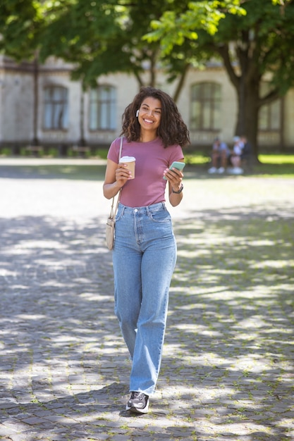 Mulata sonriente con una taza de café en las manos en el parque