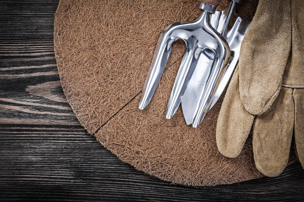 Mulchen-Kreis-Schaufel-Gabel-Lederschutzhandschuhe auf Holzbrett-Gartenkonzept.