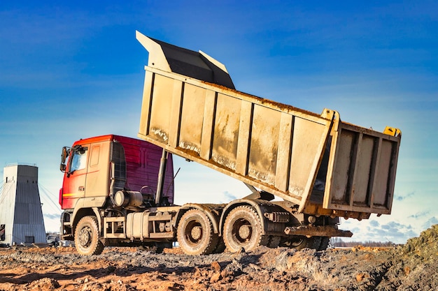 Muldenkipper mit erhöhter Karosserie auf einer Baustelle Der Prozess des Transports und Entladens von Erde Technik zum Transport von sperrigen Materialien Vermietung von Baumaschinen