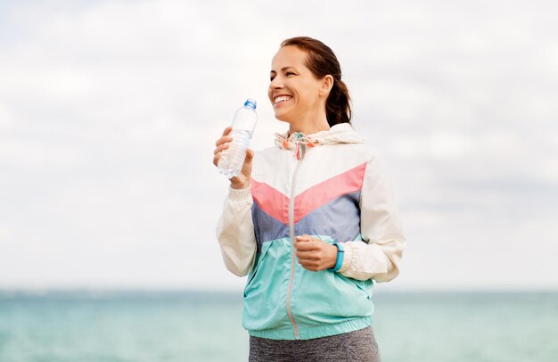 Foto mulher a beber água depois de se exercitar à beira-mar