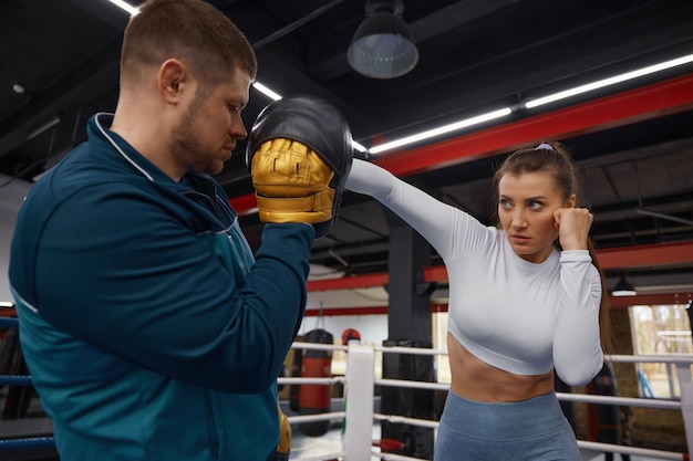 Foto mulher a dar um soco a um treinador de taebo no ginásio.