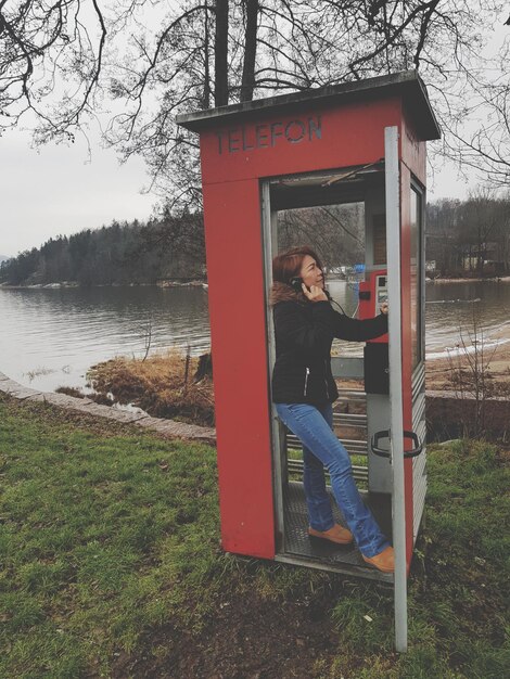 Foto mulher a falar ao telefone numa cabine telefónica ao lado do lago