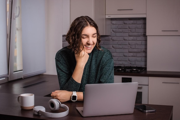 Foto mulher a falar em videoconferência no computador portátil do escritório doméstico do freelancer na cozinha