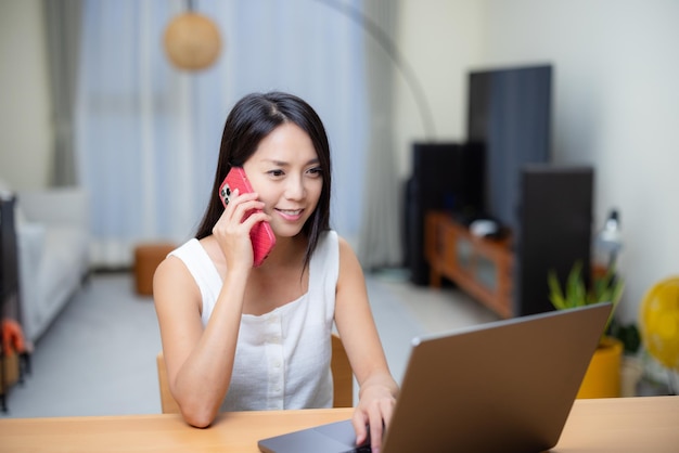 Mulher a falar no telemóvel e no portátil em casa