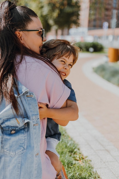 Mulher abraça um menino criança na rua. mãe e filho estão andando no parque. estilo de vida. conceito de uma infância feliz e maternidade. espaço para texto. foto de alta qualidade